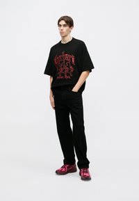 Czarna, oversize koszulka z czerwonym nadrukiem graficznym, zestawiona z czarnymi spodniami i różowymi trampkami z czarnymi akcentami. Prosty, casualowy charakter.