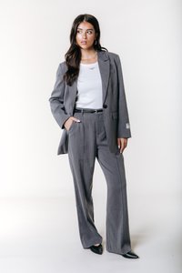 Gråstribet jakkesæt bestående af en skræddersyet blazer og brede bukser, parret med en hvid top og sorte spidse sko.