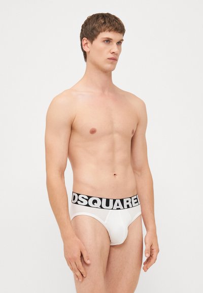 Caleçons blancs pour hommes avec une ceinture noire présentant le logo "DSQUARED" bien en vue. Le tissu semble lisse et épousant la forme.