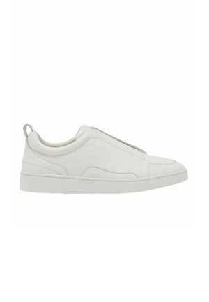 Białe niskie sneakersy typu slip-on, z wyściełanym kołnierzem i pętelką przy pięcie, wyposażone w grubą gumową podeszwę i górę ze gładkiej skóry.
