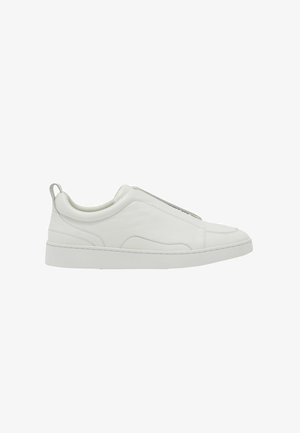 Valge madal säärega sneaker, millel on libistamisdisain, pehmendusega krae ja kandmisel drapitud aas, paks kummist tall ja sile nahast ülaosa.