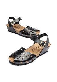 Black leather sandals featuring a perforated design, ankle strap with buckle, cork insole, and a wedge sole for support.