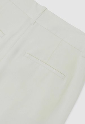 Detailný záber na biele nohavice s jedným zadným vreckom s lemom a pútkami na opasok v páse.