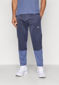 Ανδρικά παντελόνια τζόγκινγκ Nike σε σκούρο μπλε χρώμα, με πιο ανοιχτόχρωμες μπλε πάνελ. Διαθέτουν άνετη εφαρμογή, λεία υφή και μικρό λευκό λογότυπο στον μηρό.