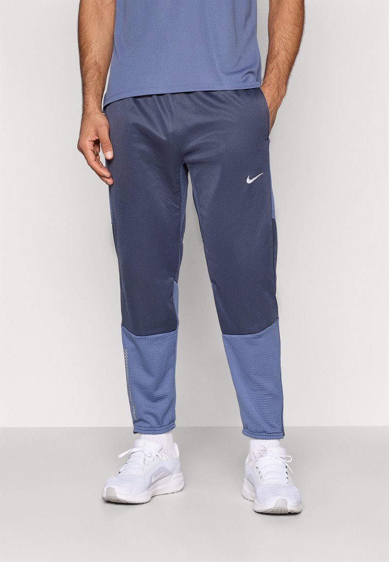 Ανδρικά παντελόνια τζόγκινγκ Nike σε σκούρο μπλε χρώμα, με πιο ανοιχτόχρωμες μπλε πάνελ. Διαθέτουν άνετη εφαρμογή, λεία υφή και μικρό λευκό λογότυπο στον μηρό.
