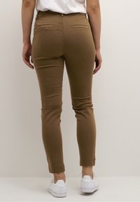 Brown tailored pants with a slim fit, featuring back pockets, a smooth texture, and a cuffed hem, paired with white sneakers.