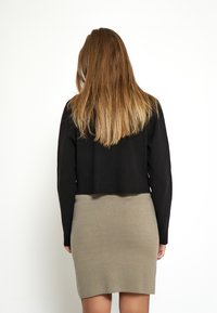 Melna cropped džemperis ar garām piedurknēm, apvienots ar pieguļošu bēšu svārku, kas izceļ gludu tekstūru. Apģērbs ir minimālists un mūsdienīgs.