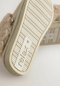 Pantoufle tan avec un dessus moelleux, texture douce et semelle à motifs avec design strié et le mot "relax" en relief.