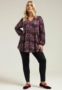 Sort bluse med livligt pink og hvidt blomstermønster, flydende design, lange ærmer; parret med sorte smalle bukser og bordeaux flade sko.