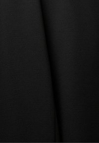 Gros plan sur un tissu noir plié avec une surface lisse, légèrement texturée, et une ombre subtile le long du pli.