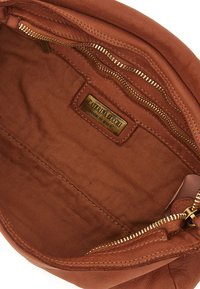 Interno di una borsa in pelle marrone con accessori dorati, dotata di una tasca con zip e un'etichetta che recita "Caterina Lucchi, Made in Italy." Fodera in tessuto testurizzato.
