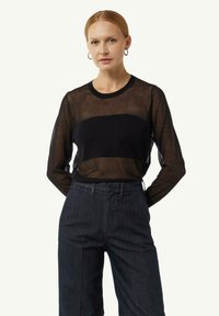 Schwarzes transparentes Langarmoberteil mit einem soliden schwarzen Mittelband, runder Ausschnitt, kombiniert mit dunklen hochgeschnittenen Hosen.