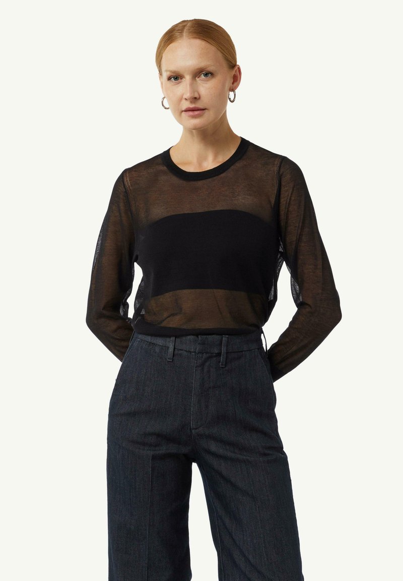 Zwarte transparante top met lange mouwen en een effen zwarte centrale band, ronde halslijn, gecombineerd met donkere high-waisted broeken.