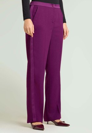 Pantalon violet à jambes larges avec des bandes latérales, doté d'une fermeture par bouton et de poches. Porté avec des chaussures bordeaux à bout pointu.