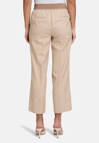 Beżowe, szerokie spodnie z teksturowanym paskiem w talii, tylnymi kieszeniami i gładkim wykończeniem, w połączeniu z jasnymi sandałami na obcasie.