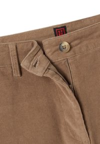 Pantalon en velours côtelé marron avec bouton, fermeture éclair partiellement ouverte, passants de ceinture et petite étiquette de marque rouge et noire visible à l’intérieur de la ceinture.