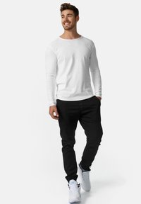 Camisa blanca de manga larga combinada con pantalones negros y zapatillas blancas. Ajuste casual, textura suave y diseño simple.