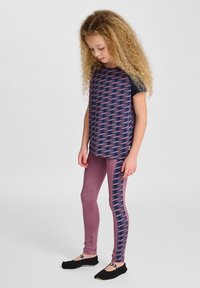 Flerfärgad träningsoutfit med en marinblå topp med rosa zigzag-mönster och matchande rosa leggings med sidodesign. Svarta skor.