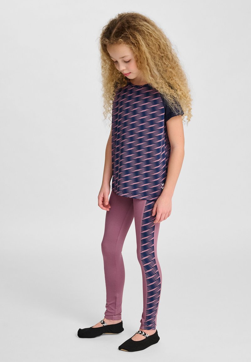 Flerfärgad träningsoutfit med en marinblå topp med rosa zigzag-mönster och matchande rosa leggings med sidodesign. Svarta skor.