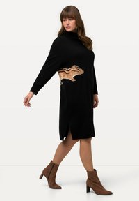 Abito nero a maglia con colletto alto, caratterizzato da una grafica di animale color sabbia sul lato e spacco laterale. Abbinato a stivali alla caviglia marroni.