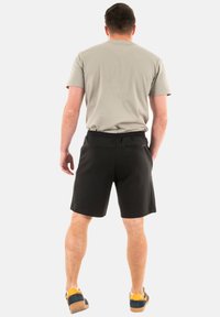 Pantaloni sportivi neri con elastico in vita, abbinati a una maglietta grigia chiara. I pantaloni presentano una tasca laterale e una texture liscia.