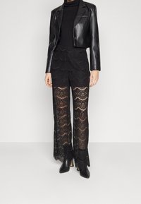 Zwarte kanten wijde broek met een geschulpte zoom, gecombineerd met een strakke zwarte coltrui en een korte zwarte leren blazer.