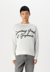 Light grey knitted sweater featuring a black cursive text design reading "Sporting Goods & Equipment," with ribbed cuffs and hem.
