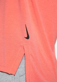 Koraliowa koszulka Nike z krótkim rękawem, z czarnym logo, wykonana z lekkiego materiału, z bocznymi rozcięciami dla lepszej wentylacji i swobody ruchów.