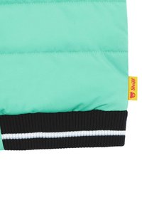 Helle teal Pufferjacke mit horizontaler Naht und einem schwarzen gerippten Bund mit weißen und grauen Streifen; gelbes Markenschild angebracht.