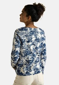 Pikend varrukatega särk, millel on sinine ja valge botaaniline trükk, ümara kaelusega ja mugava lõikega. Kangas näib olevat pehme ja tekstureeritud.