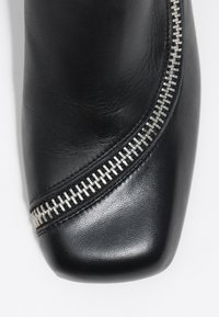 Juodasis odinis kulkšninis botas su kvadratiniu pirštu, su dekoratyviniu sidabriniu užtrauktuku šone, lygia tekstūra ir elegantišku dizainu.