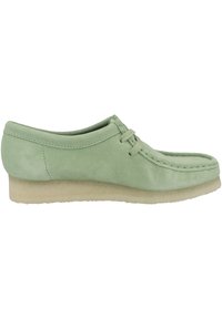 Scarpa in suede verde chiaro con punta rotonda, design con lacci e suola bassa in gomma beige texture. Cuciture sottili attorno alla parte superiore.