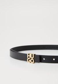 Curea din piele neagră cu un design elegant, dotată cu un sistem de închidere cu hardware în ton auriu cu logo-ul "HUGO", textură netedă și găuri uniform distribuite.
