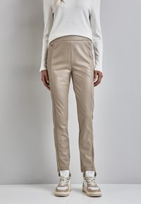 Beige neplederen broek met een slim fit, voorzien van zijdelingse naden, en gecombineerd met beige en witte sneakers. Soepele textuur en modern ontwerp.