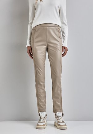 Beige konstläderbyxor med slim fit, med sidosömmar och matchade med beiga och vita sneakers. Slät textur och modern design.