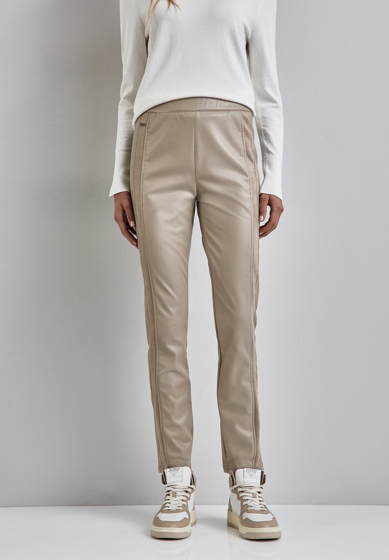 Beige neplederen broek met een slim fit, voorzien van zijdelingse naden, en gecombineerd met beige en witte sneakers. Soepele textuur en modern ontwerp.