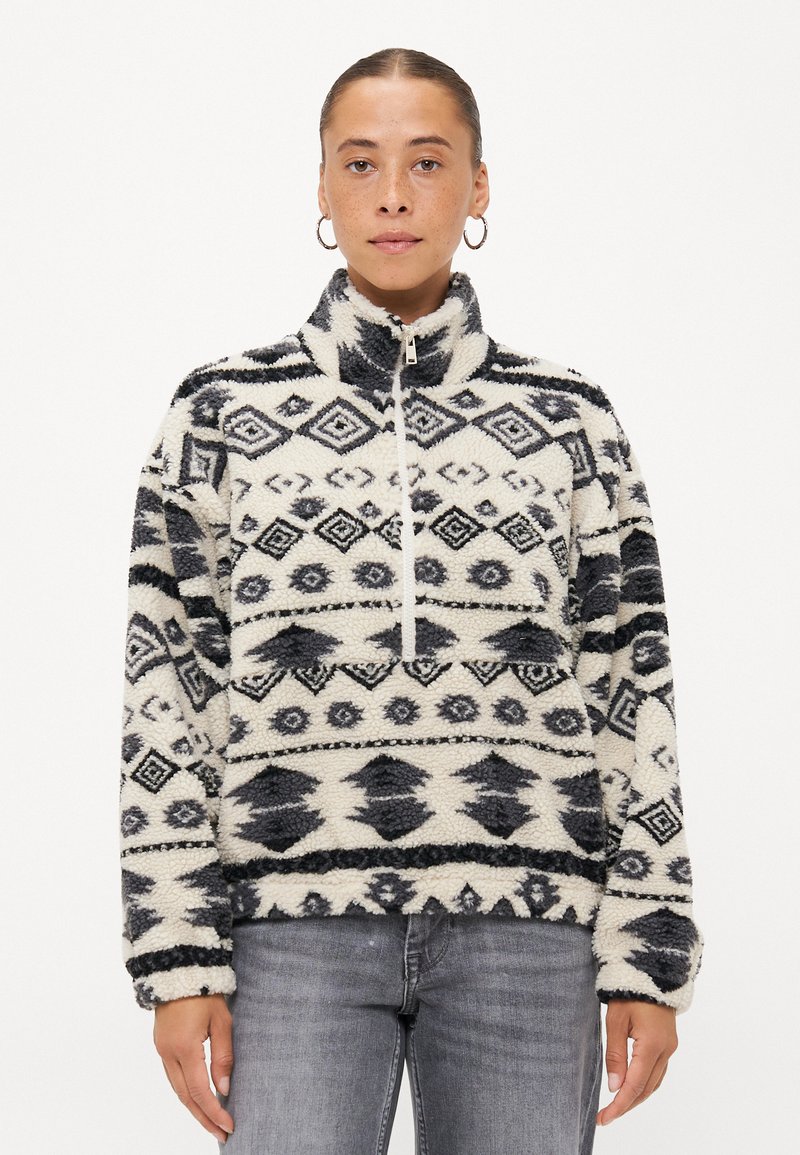 Pull en polaire avec col haut, présentant un motif géométrique noir et blanc. Fermeture éclair et poignets élastiques. Texture douce.