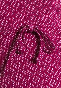 Fuksjowa tkanina z białym geometrycznym wzorem, związaną sznurkiem w pasie. Tekstura wydaje się gładka i lekko elastyczna.