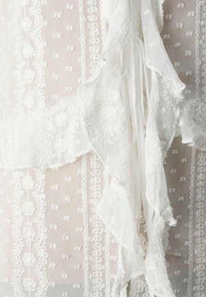 Tissu de robe blanche avec une délicate bordure en dentelle, des motifs floraux brodés et des accents volantés, d'une texture transparente et d'un design en couches.