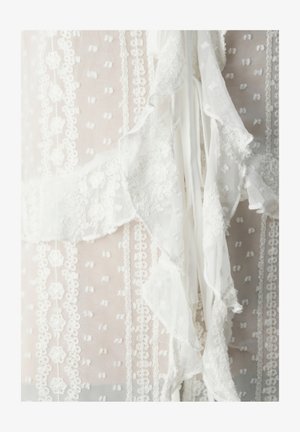 Tissu de robe blanche avec une délicate bordure en dentelle, des motifs floraux brodés et des accents volantés, d'une texture transparente et d'un design en couches.