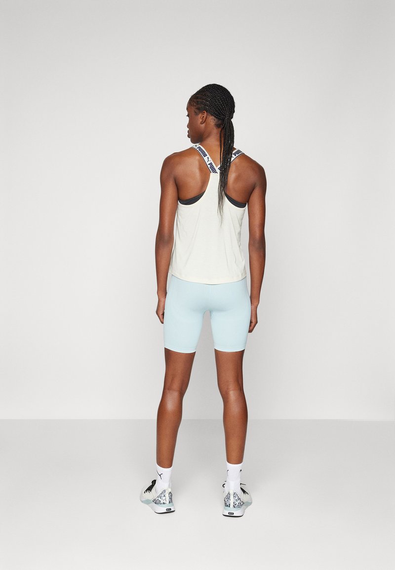 Top in crema leggero senza maniche con un cinturino decorato, abbinato a pantaloni corti azzurri. Le sneakers presentano un motivo decorativo sul tacco.
