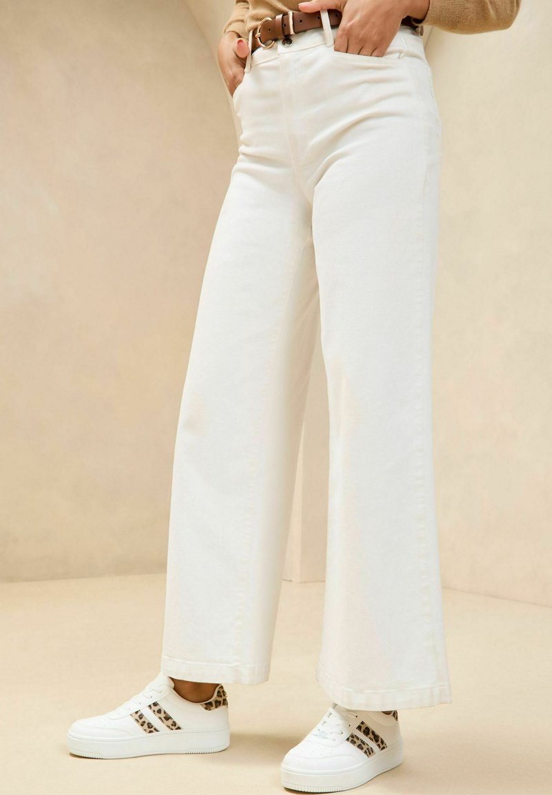 Jeans bianchi a gamba larga in cotone, con tasche frontali e vita alta, abbinati a sneakers bianche con accenti in stampa leopardata.
