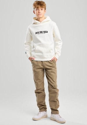 Witte hoodie met de opdruk "INTO THE WILD" en een buidelzak, gecombineerd met kaki broek en witte sneakers. Soepele stof en een relaxte pasvorm.