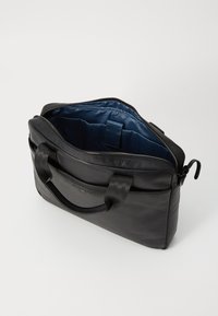 Svart lærveske med glidelås på toppen, teksturert overflate, polstrede håndtak og blå innvendig fôr. Har en frontlomme og innvendig organisering.