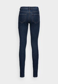Mørkeblå denimjeans med en tettsittende fasong, som har to baklommer, midjehøyde og kontrasterende sømmer. Jeansen har en jevn tekstur og klassisk design.