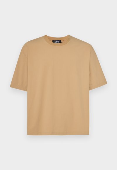 T-shirt di cotone beige con scollo rotondo, maniche corte e vestibilità rilassata. Texture liscia con cuciture lungo l'orlo e le maniche.