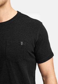 Sort crew neck t-shirt med korte ærmer, der har en lomme på brystet og et lille mærke. Fremstillet af blødt, tekstureret stof.