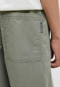 Olijfgroene korte broek van katoen met een achterzak met zichtbare stiksels en een zwart label met de tekst "JACK & JONES." Glad van structuur.