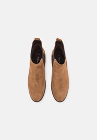 Botas de tobillo de ante marrón con paneles laterales elásticos, punta redondeada y una lengüeta para facilitar el calzado. Textura suave y diseño aerodinámico.
