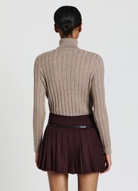 Beige gerippter Strickpullover mit hohem Kragen, kombiniert mit einem dunkelbraunen Faltenrock, der einen Bund mit schwarzem Akzent präsentiert.